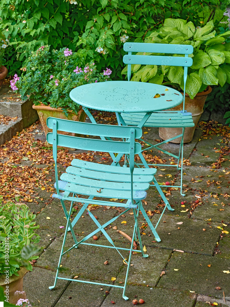 Green courtyard metal chairs and table in a serene, peaceful, lush, private backyard at home on a su