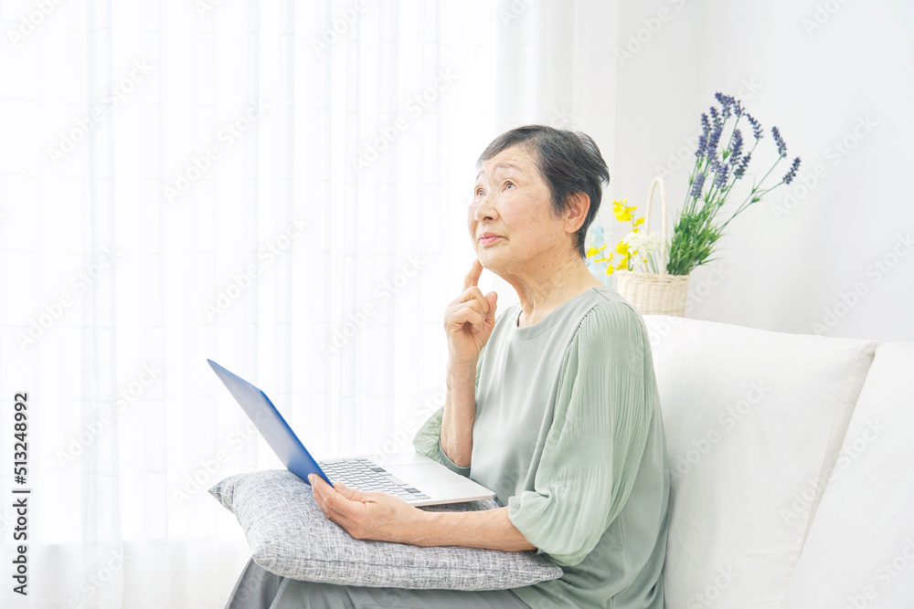 リビングでノートパソコンを持って考える高齢者女性