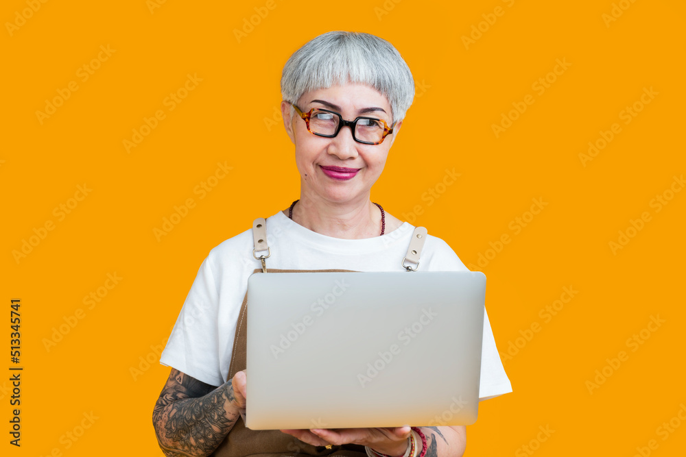 资深老年女性纹身企业主系围裙手提笔记本电脑人像微笑，网络营销