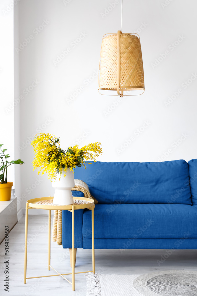 桌子上放着含羞草花的花瓶，客厅里放着蓝色沙发