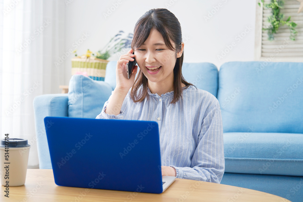 リビングでノートパソコンを見て電話する女性