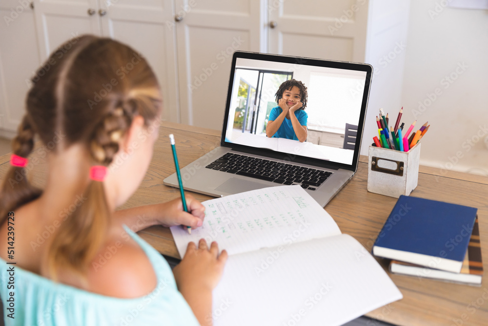 高加索女孩在笔记本电脑上与混血朋友通过视频通话在线学习时写笔记