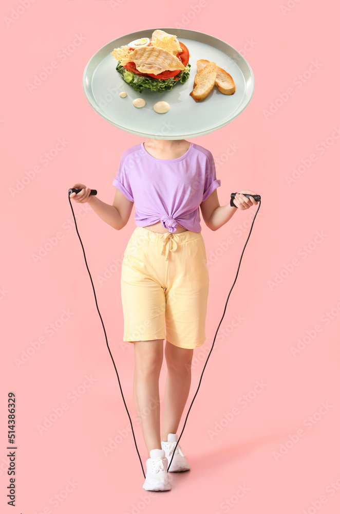 运动型年轻女子，带着跳绳和一盘美味的凯撒沙拉，而不是她的头放在粉红色的ba上