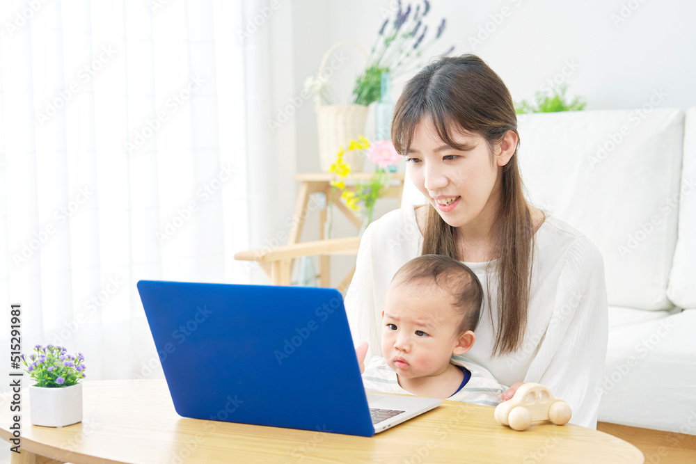 リビングで赤ちゃんとノートパソコンを見る母親