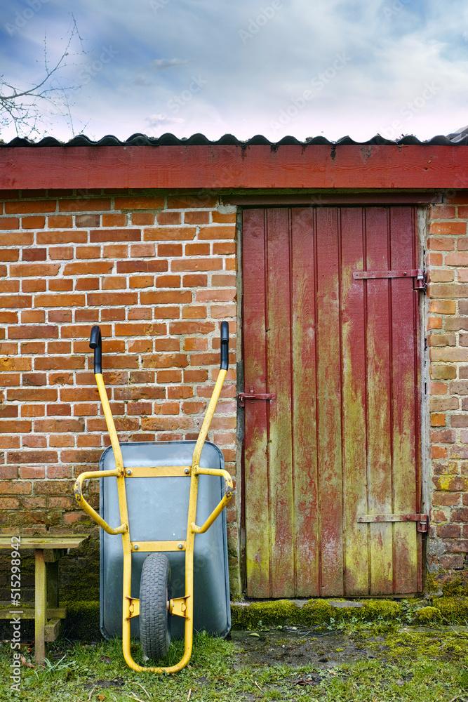 A shot of an upside-down wheelbarrow, a small brick farmhouse with a red and yellow mixed-painted do