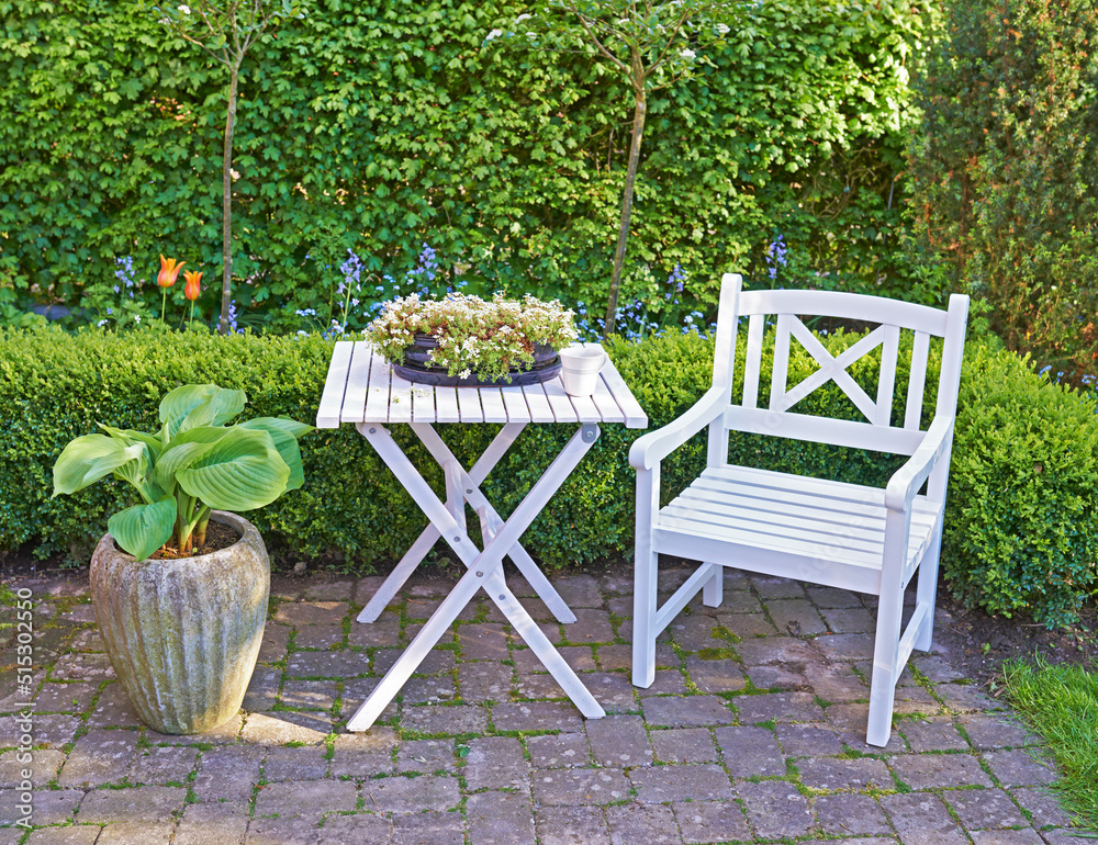 绿色花园里的白色木制椅子和桌子，花园里有开花的植物和复制空间。宁静的风景
