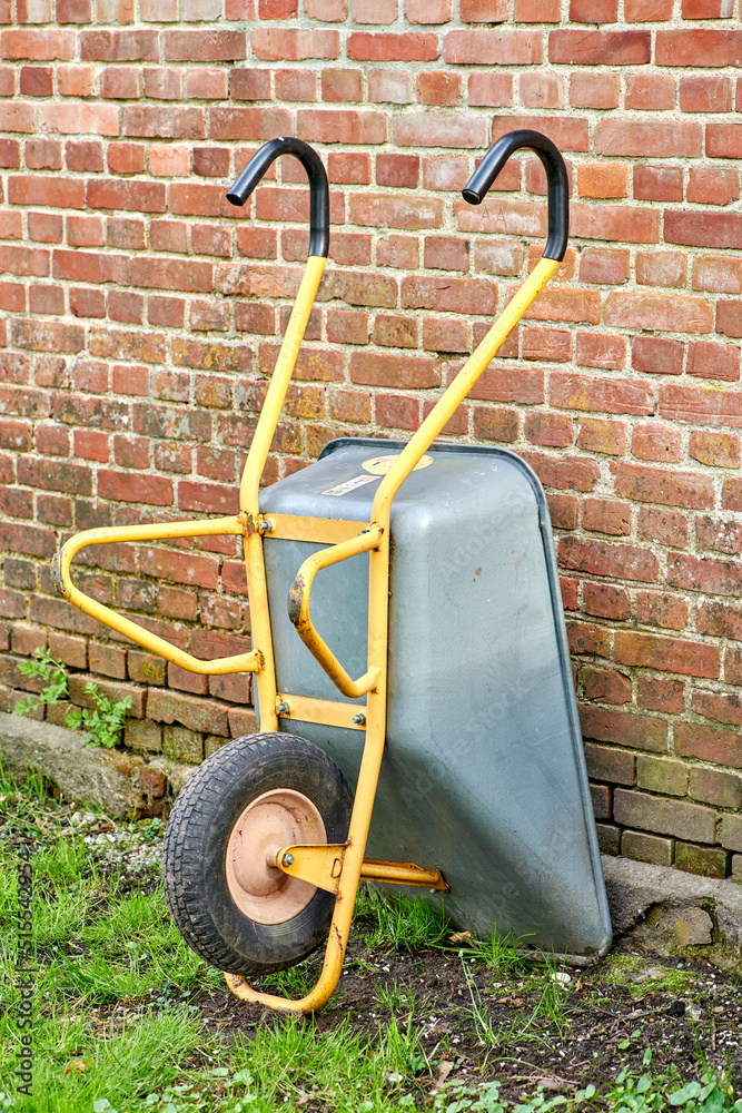 手推车靠在红砖墙或房子的一侧。在后面做园艺或清理工作