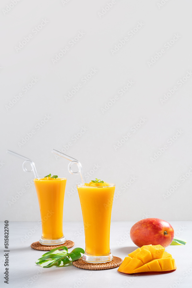 在灰色桌子背景上的玻璃杯中，新鲜美味的芒果汁奶昔。