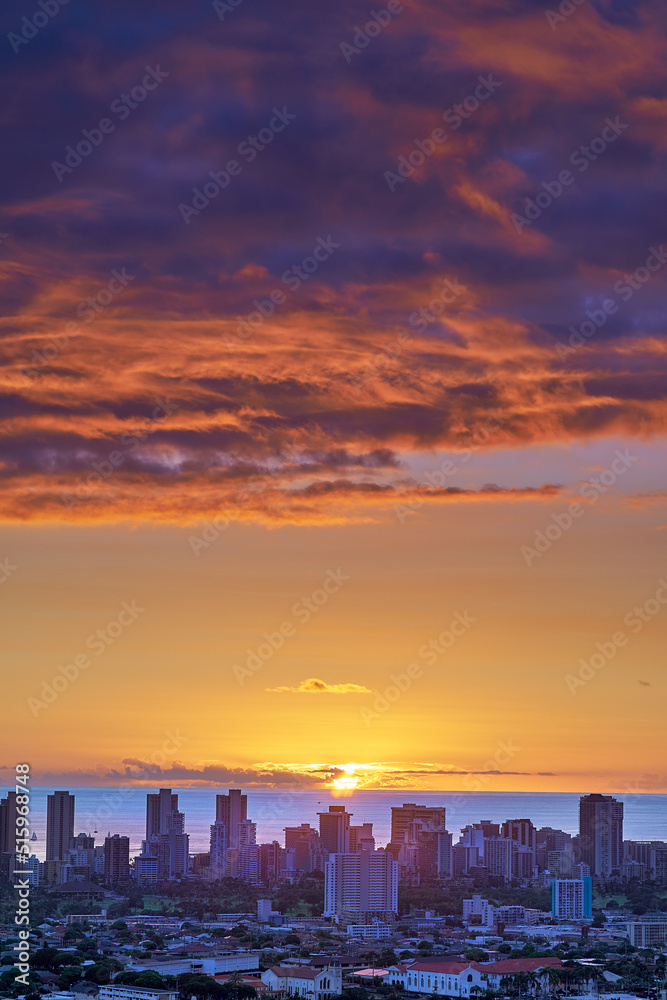 日落在海边的城市天际线上，多云的紫色和橙色天空。日出在蓝色的地平线上