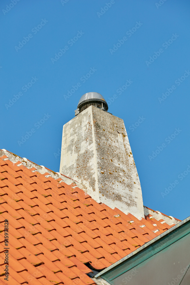 混凝土烟囱设计在石板屋顶或建筑外部，背景是晴朗的蓝天。