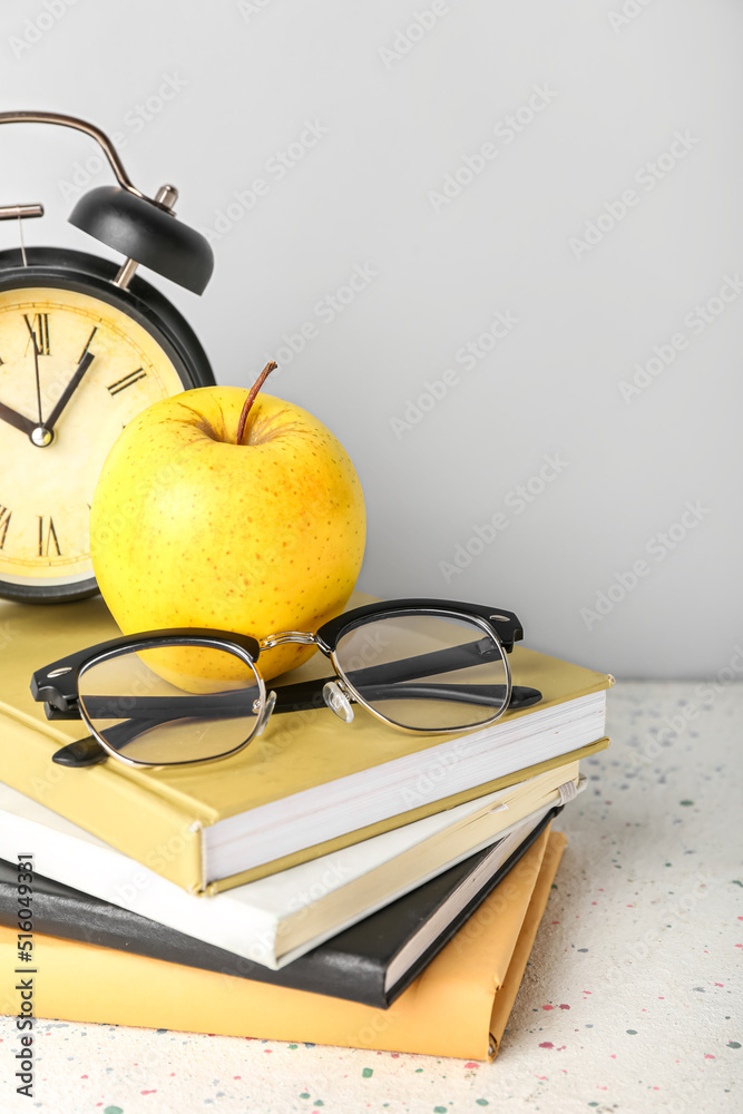 灰色背景下，桌子上放着苹果、眼镜和闹钟的学校书籍