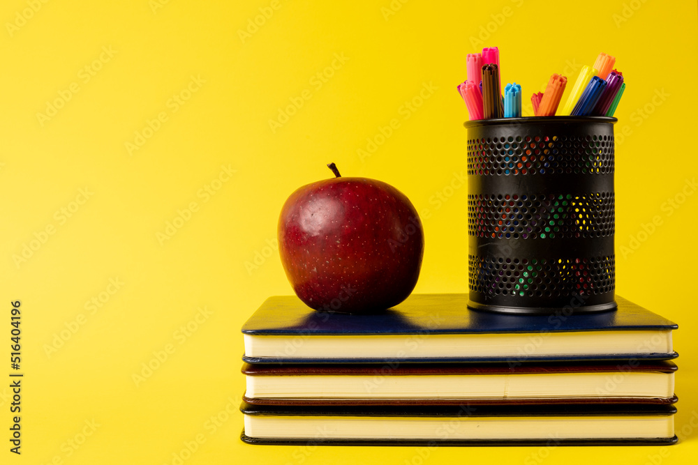 一叠书、容器中的毡尖笔和黄色背景上的苹果的组成
