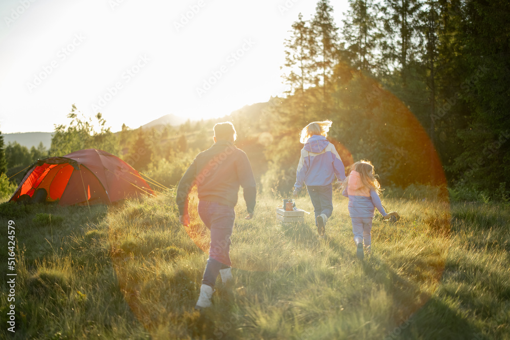 年轻的高加索家庭带着小女孩一起走在绿色的草地上，带着帐篷旅行