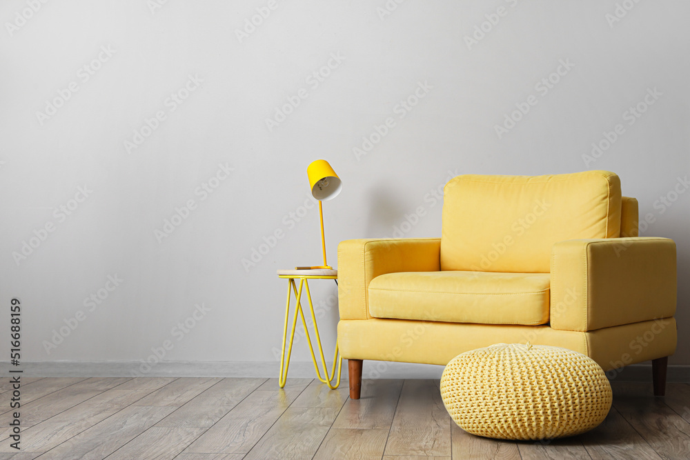 舒适的扶手椅，靠近房间的浅色墙壁，配有桌子、灯和脚凳