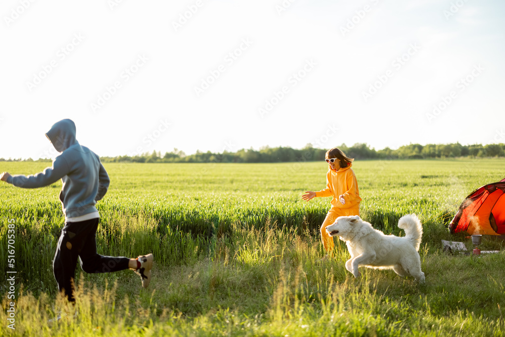 年轻夫妇和他们的狗玩耍，在大自然中带着帐篷愉快地度过夏天。兰