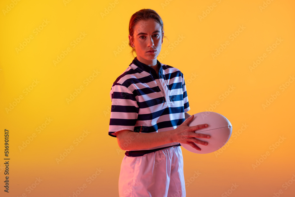 Portrait of caucasian female rugby player with rugby ball over neon yellow lighting