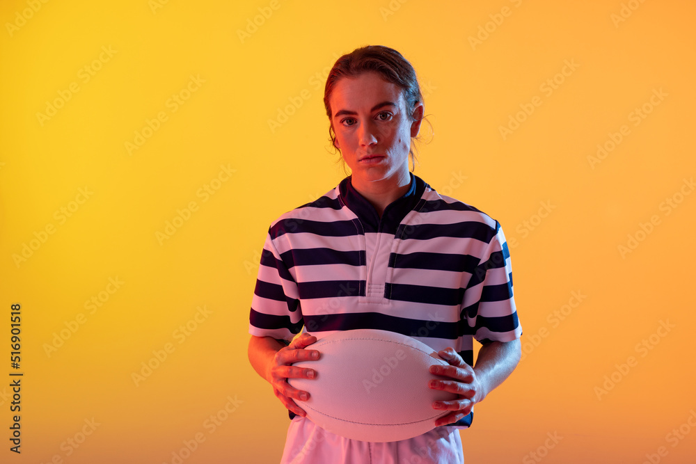 霓虹黄灯下拿着橄榄球的高加索女橄榄球运动员的肖像