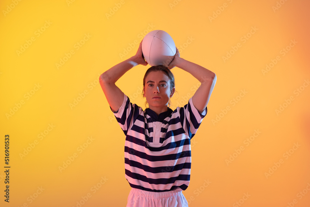 在霓虹黄灯下拿着橄榄球的高加索女橄榄球运动员的肖像