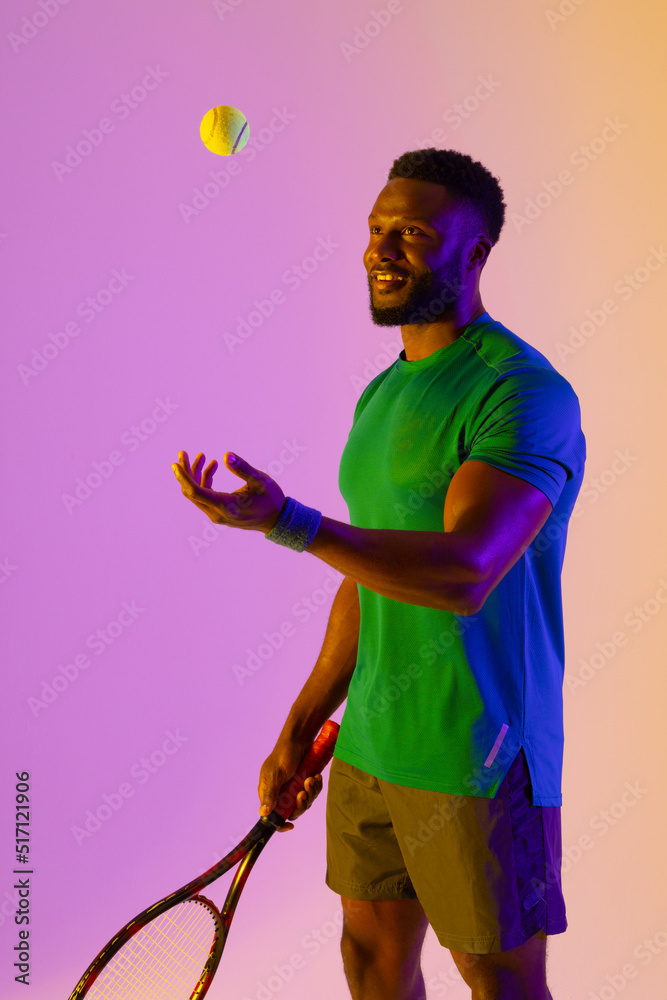 紫色和黄色霓虹灯下快乐的非裔美国男子网球运动员的垂直图像