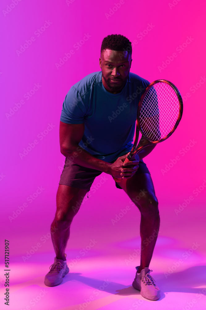 紫色和粉色霓虹灯下快乐的非裔美国男子网球运动员的垂直图像