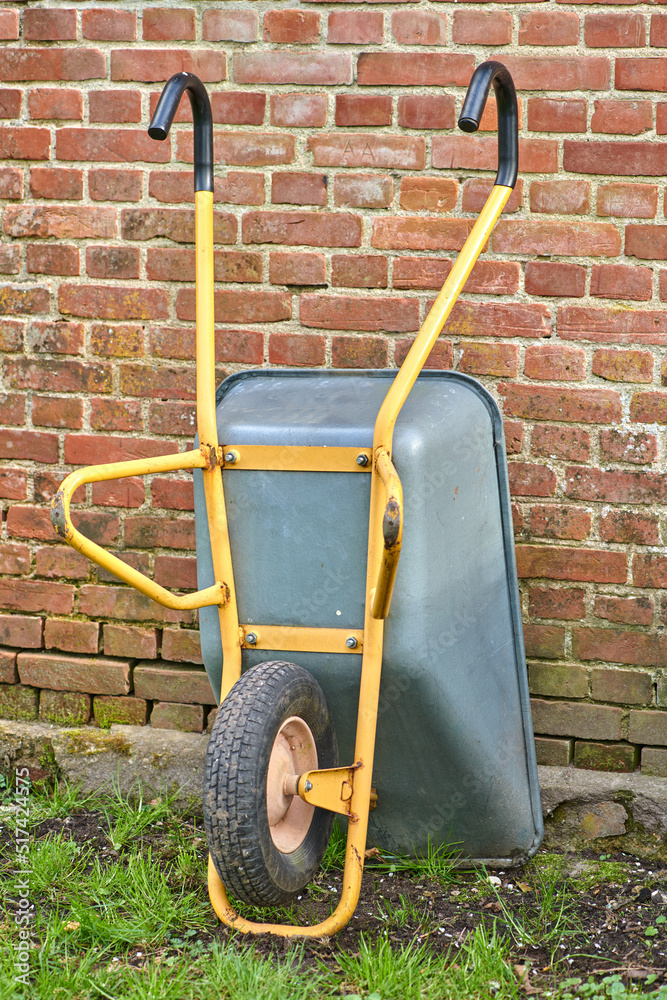 Garden wheelbarrow leaning against a red brick wall in a home backyard. Landscaping equipment and to