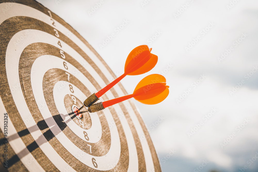 Close up shot red darts arrows in the target  of dartboard center on dark blue sky background. Busin