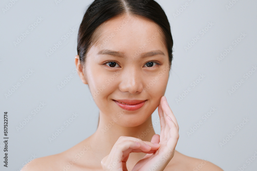 年轻的亚洲女性在灰色背景下触摸健康的面部美容皮肤。