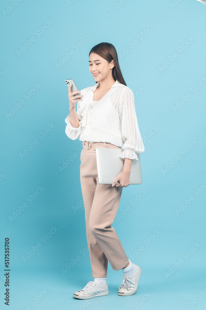 年轻漂亮的亚洲女人穿着漂亮的休闲布，使用蓝色背景隔离的智能手机