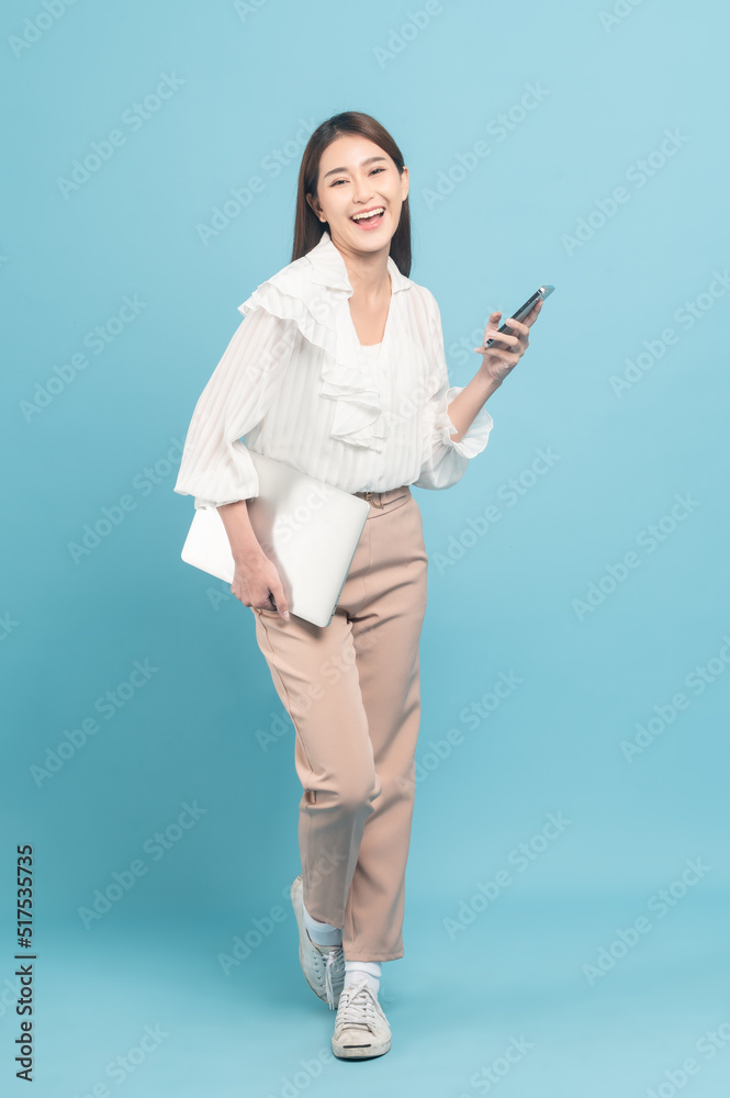 年轻漂亮的亚洲女人穿着漂亮的休闲布，使用蓝色背景隔离的智能手机