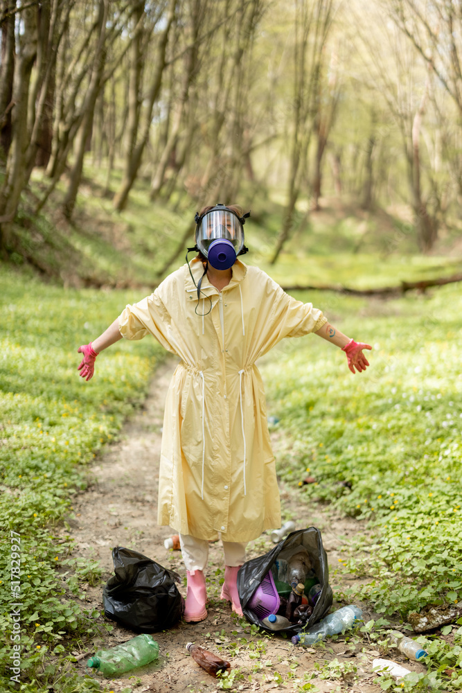 一名戴着防毒面具、穿着防护服的妇女站在垃圾袋里收集散落的塑料