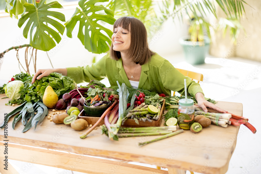 一个年轻快乐的人坐在桌子旁，桌上摆满了新鲜的蔬菜、水果和绿色蔬菜。
