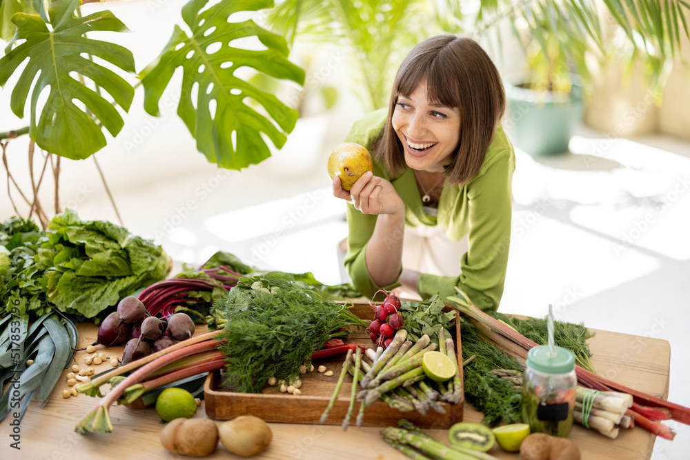 一个年轻快乐的女人的肖像站在摆满新鲜蔬菜、水果和绿色蔬菜的桌子旁