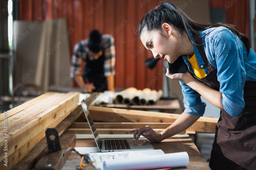 年轻的亚洲女木匠在woodcra与客户通电话时使用笔记本电脑