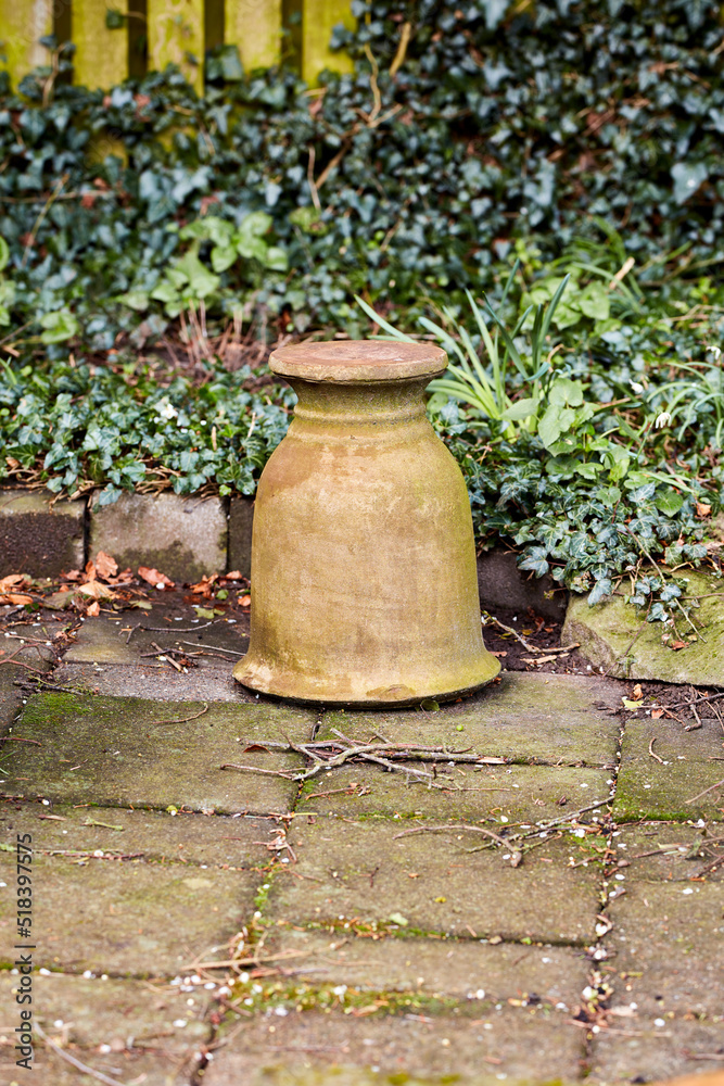 花园里的罐子。花园地板上的一个陶瓷壶，背靠绿色的灌木丛。一个空的、weathe的细节