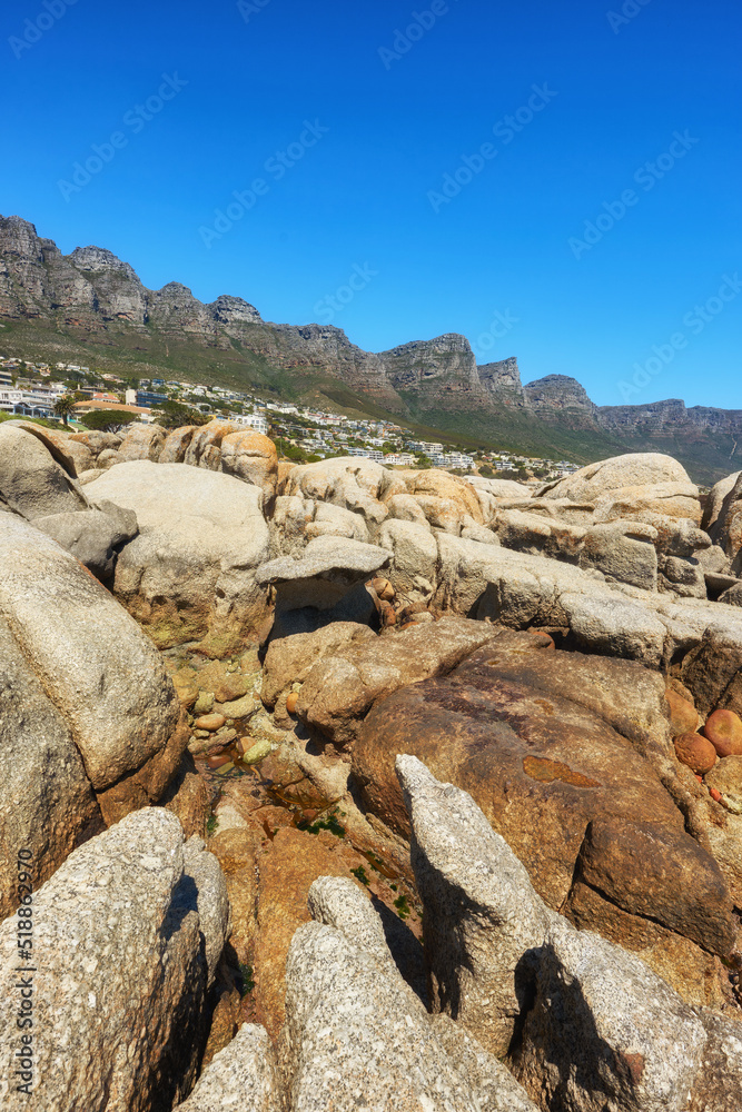 Coastal rocks with view of the mountains and city on blue sky background with copy space. Bright sum