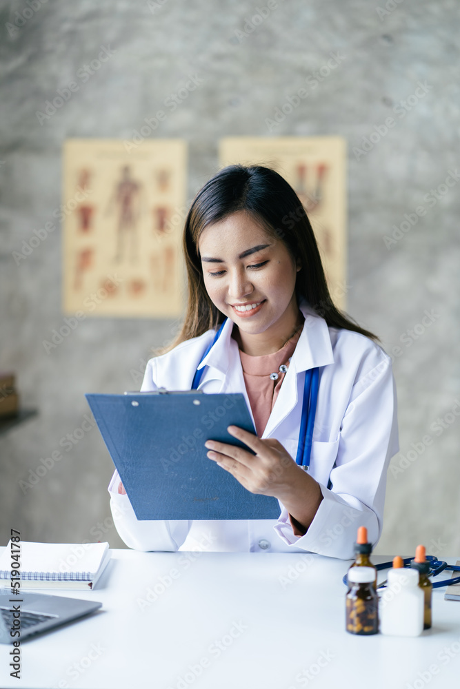 微笑的年轻亚洲女医生在诊所接待处工作，她正在使用电脑和书写