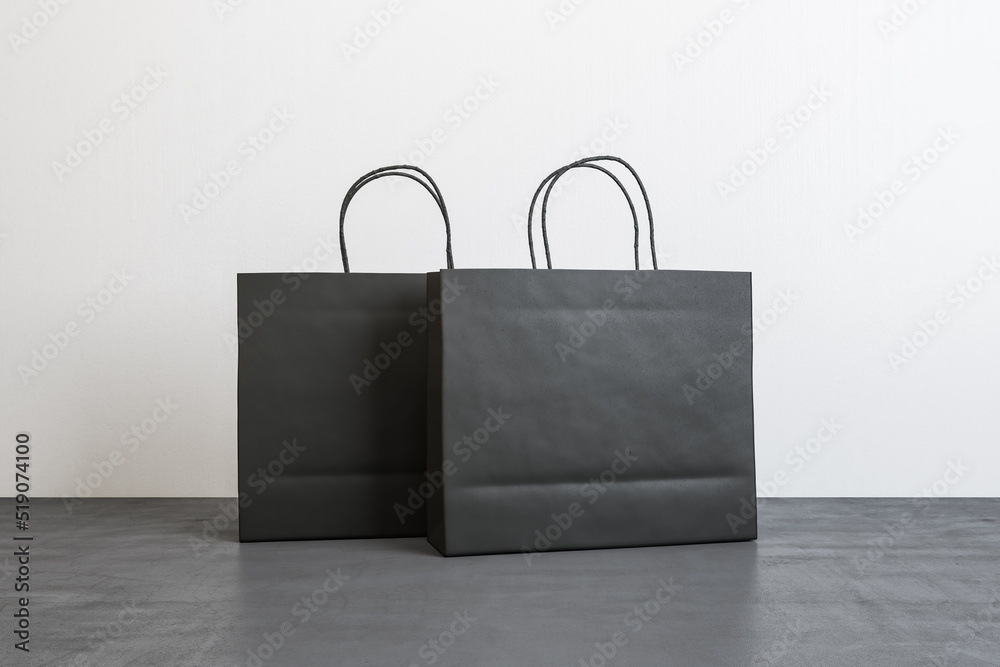 两个空白的黑色纸袋，在白墙上的混凝土地板上放置您的标志或文字