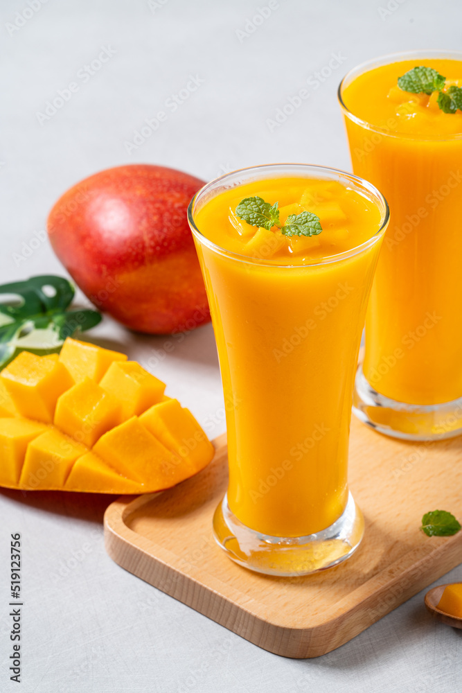 在灰色桌子背景上的玻璃杯中，新鲜美味的芒果汁奶昔。