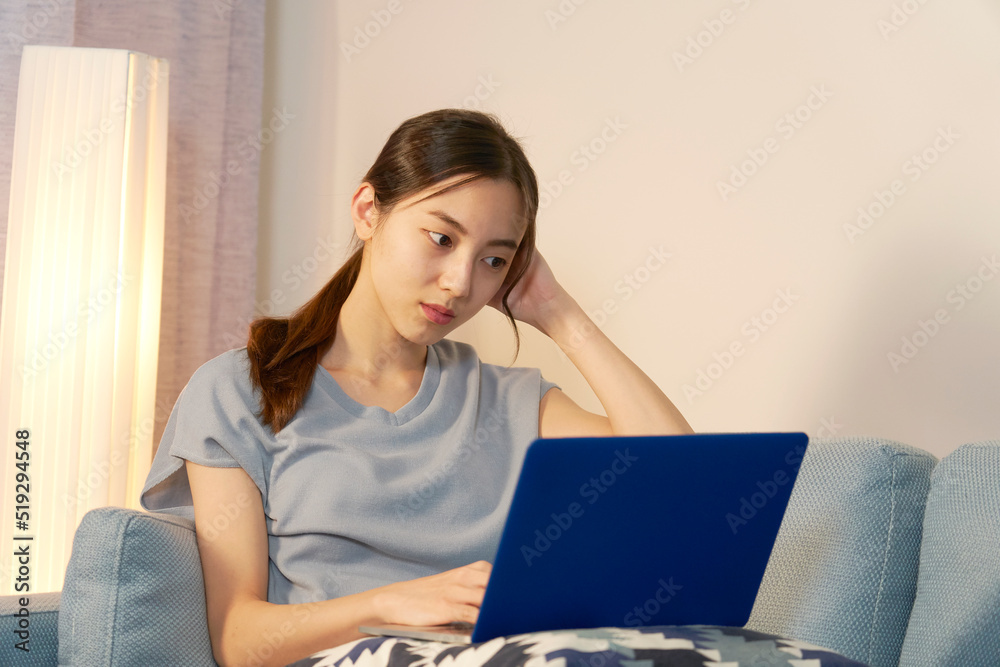 夜にリビングでパソコンを見て考える女性