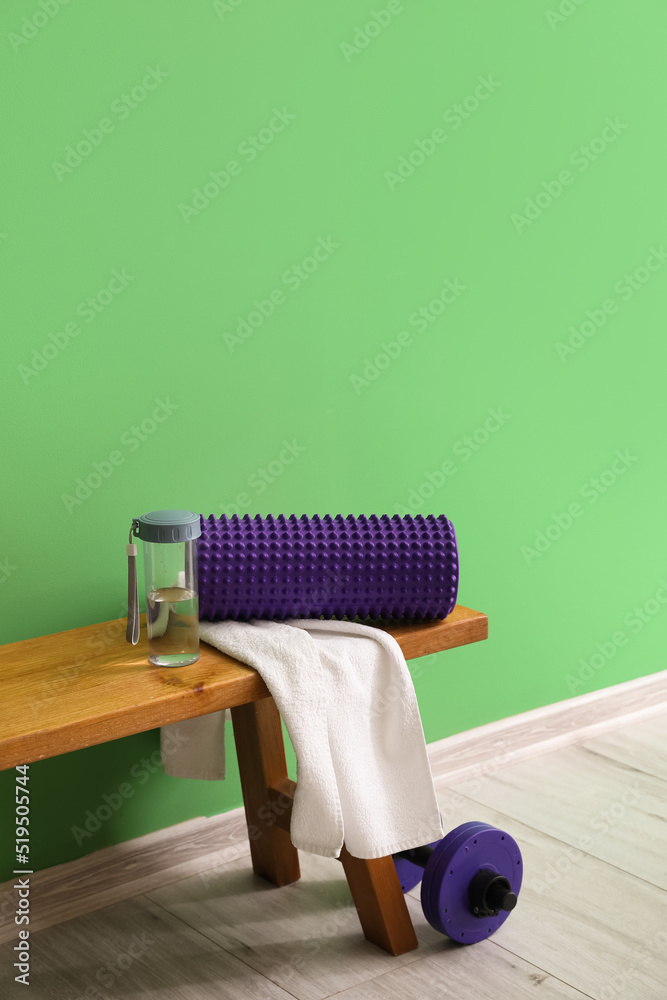 带毛巾和水瓶的泡沫滚筒放在靠近绿墙的长凳上
