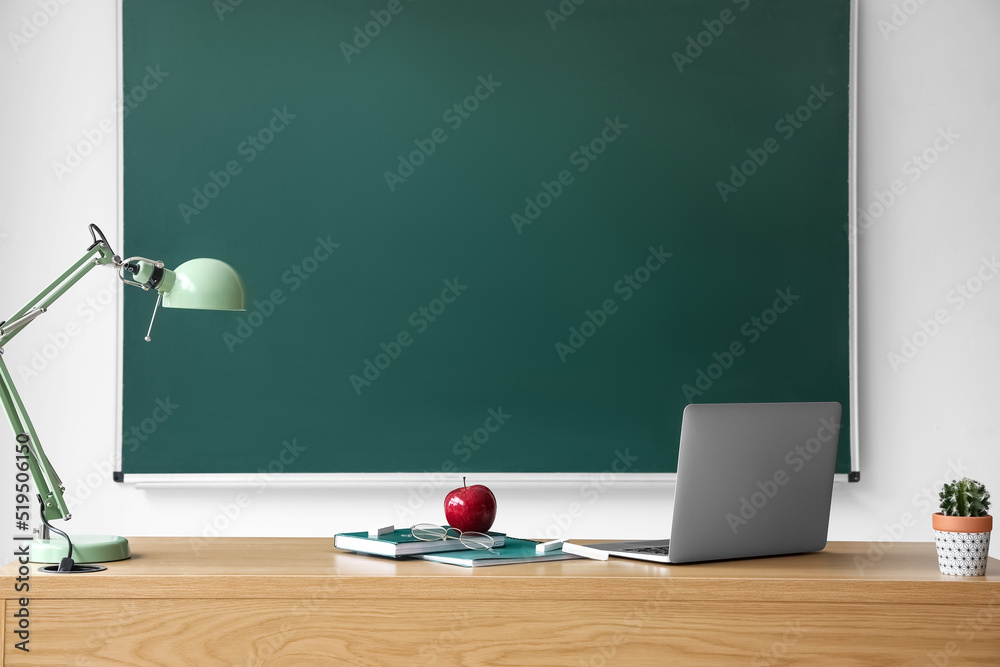 黑板附近的桌子上有书、眼镜、笔记本电脑和灯的苹果