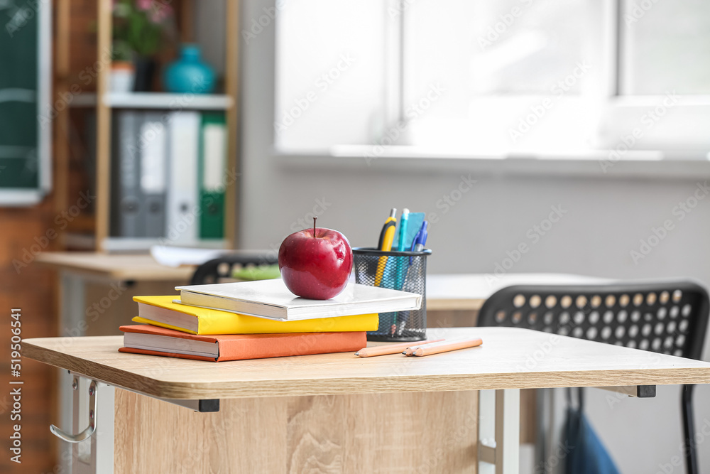 教室桌子上放着书、笔杯和学校文具的苹果