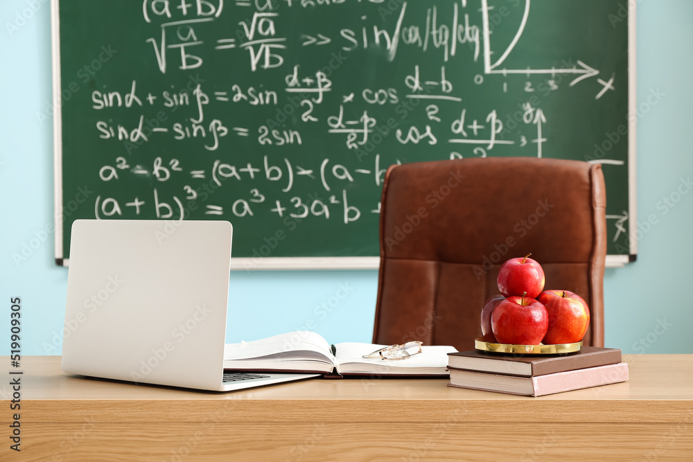 教室桌子上放着苹果、书、眼镜和笔记本电脑的盘子