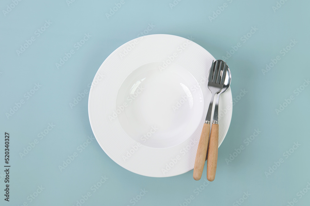 浅蓝色背景上有叉子和勺子的空白色陶瓷菜，美食概念