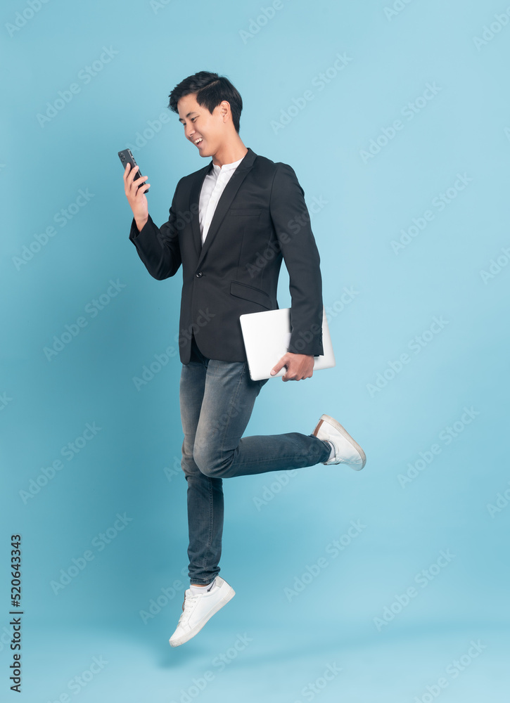 Young asian businessman in smart casual style using smartphone and holding a laptop jumping isolated
