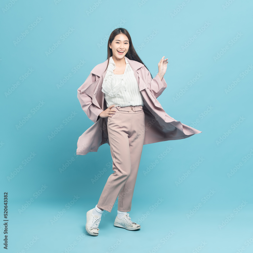 Young beautiful asian woman with smart casual cloth wearing pink coat smiling isolated on blue backg