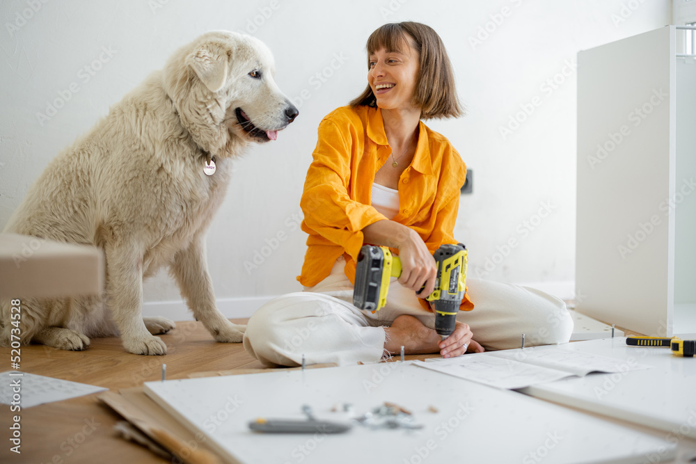 年轻女子自己组装家具，坐在新公寓里和她的可爱小狗玩得很开心