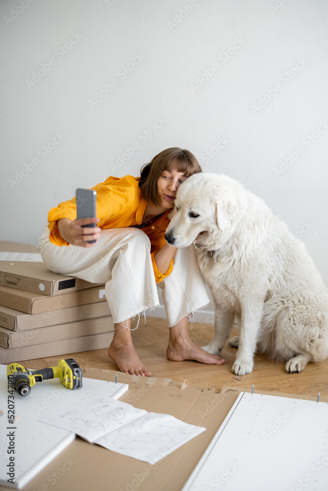 Young woman makes selfie photo on phone with her cute dog, have fun while making repairing at new ap