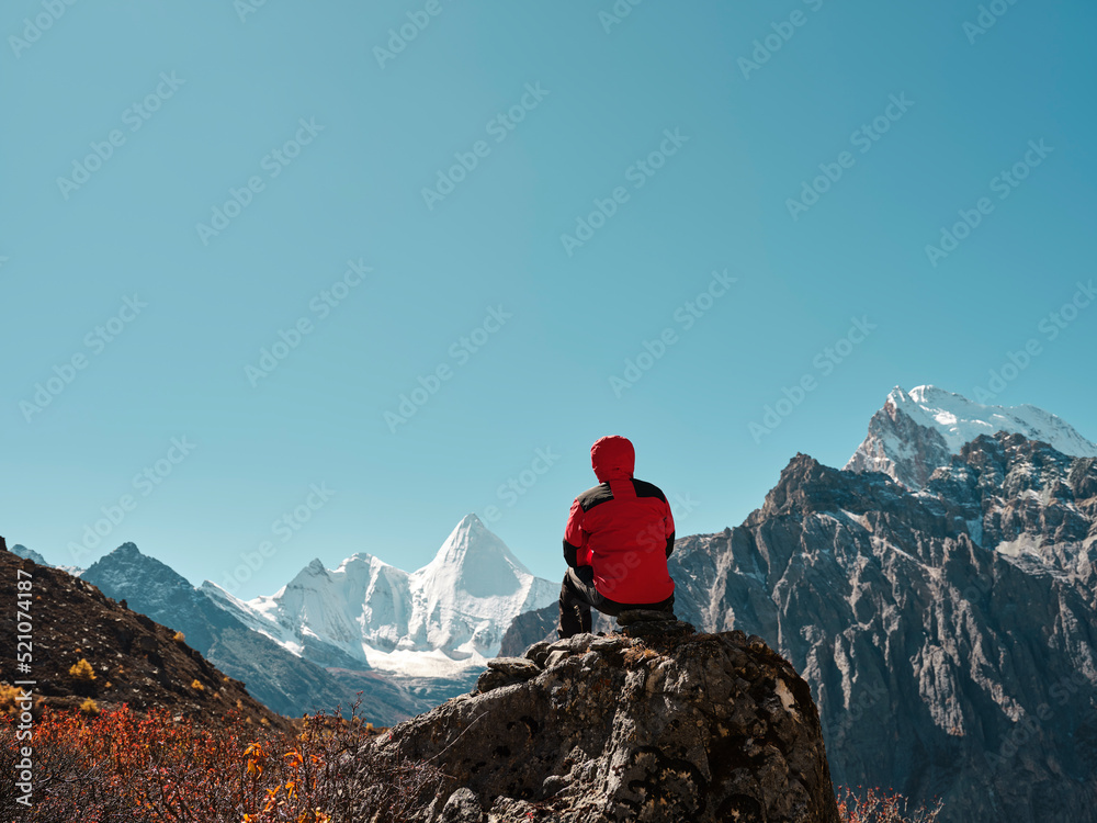 asian man sitting on top of rock looking at view with Mount Yangmaiyong (or Jampayang in Tibetan) in
