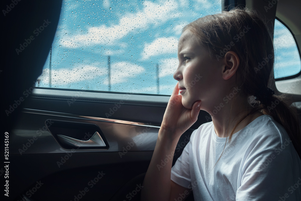 Pensive girl sits in car on backseat feeling sadness on rainy summer day. Teenager props head up wit